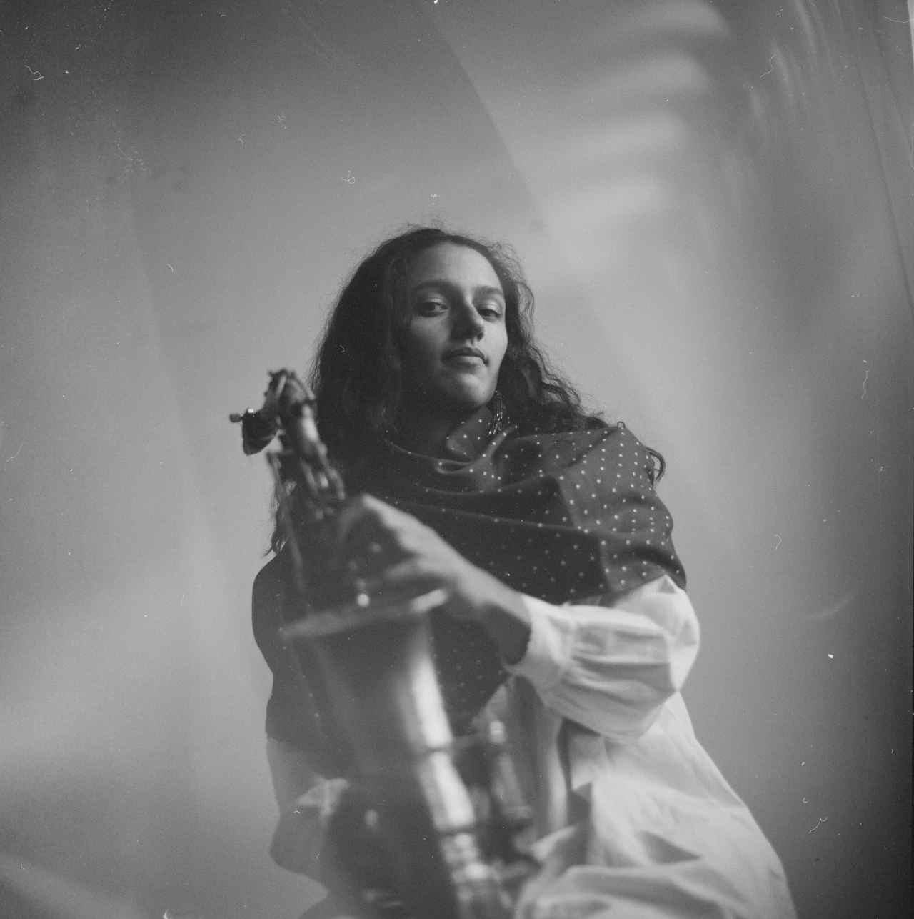 Black and white picture of Sara El Hachimi'looking down to the camera holding her saxophone